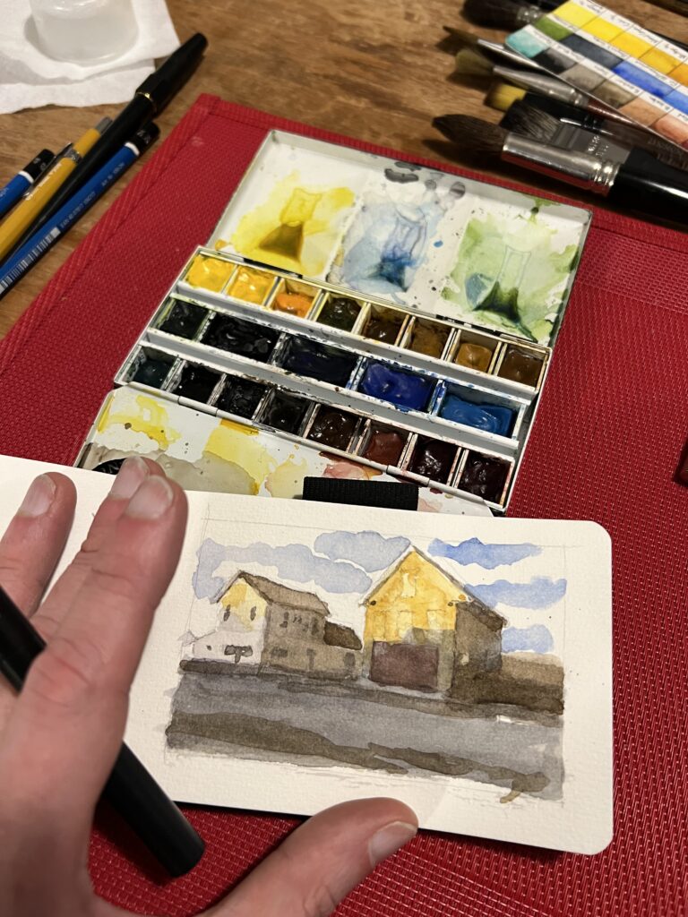 Small watercolour painting of buildings on Lorne Street in Sackville, New Brunswick. The sketchbook is sitting on a watercolour palette.